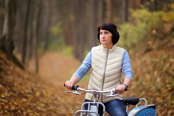 Fototapeta na wymiar The girl on a bike from the rental in the forest. Beautiful young woman posing for the camera in the autumn forest. 