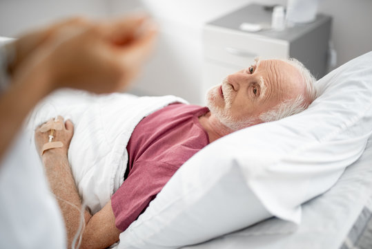 Portrait of male patient lying in bed and looking at doctor. He is receiving intravenous treatment