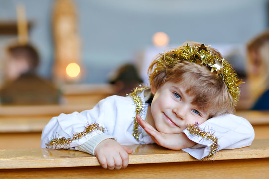 Beautiful little kid boy playing an angel in Christmas story in a church. Happy adorable blond child with lights and xmas tree on background. Celebration of Xmas eve, big christian, catholic holiday.