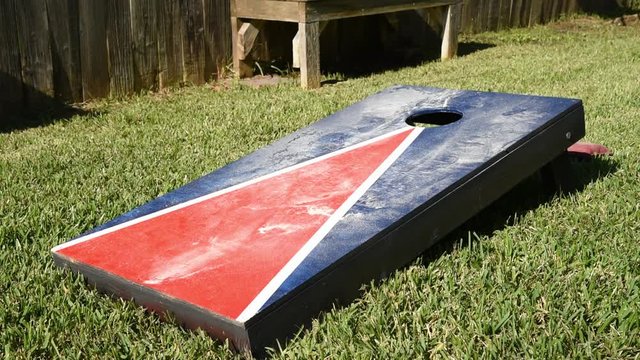 Home made red white and blue corn hole game with maroon and orange bags landing on dusty board