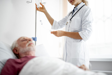 Cropped portrait of young lady in white lab coat adjusting infusion bottle in hospital room....