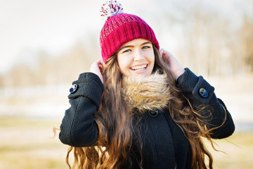 Cute cheerful teenage girl with long hair, wearing winter outfit, outdoors at park. Natural...