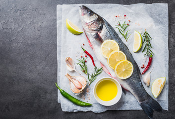 Fresh fish sea bass and ingredients for cooking. Raw fish sea bass with spices and herbs on black slate table copy space.