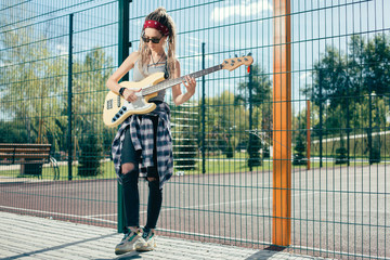 Talented young lady playing the guitar while being at the sports ground