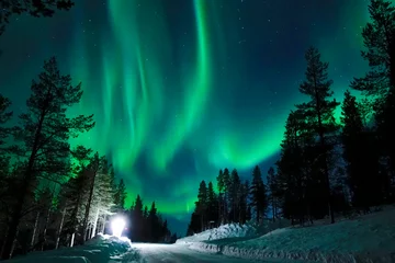 Wall murals Northern Lights Bright lamp shining on the empty snowy road just as the northern lights appear.