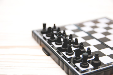 small pocket chess, plastic chess pieces placed on a chessboard on a white wooden background