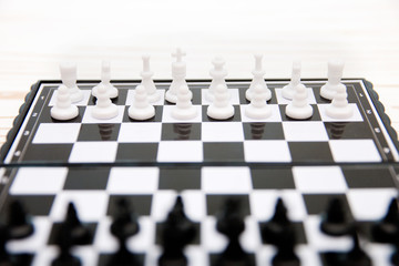 small pocket chess, plastic chess pieces placed on a chessboard on a white wooden background