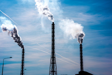 Industrial pipes with smoke against blue sky