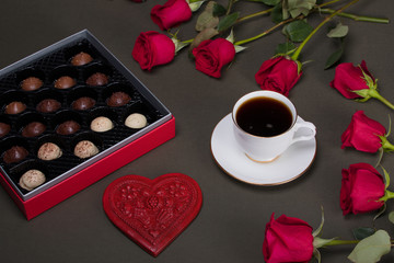 Dark and light chocolate candy in a red box next to red roses, heart, and cup of coffee