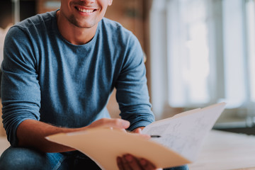 Close up of smiling guy is sitting in office while hilding folder of documents
