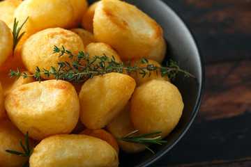 Roast golden potatoes seasoned with salt, garlic, rosemary and thyme on rustic wooden background