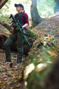 Soldier girl with a gun in the forest/Woman with rifle in her hands and a black  body armor in the forest. Low angle shooting