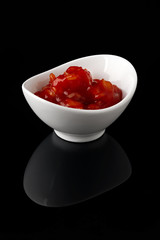 Sauce in a white bowl on a black background with reflection.