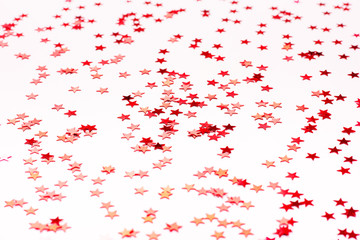Beautiful festive white background with red metallic star shaped confetti. Holiday or decoration concept.