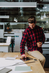 Obraz premium Delighted young bearded man sitting on the table while surfing the internet in the tablet