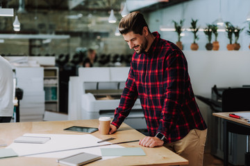 Positive handsome smiling man standing near table while working in the office