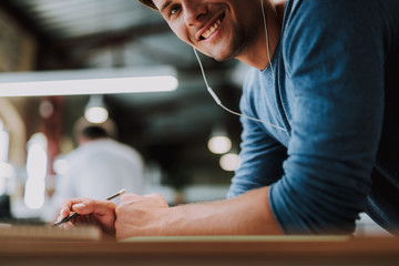 Close up of a delighted handsome man listening to music while writing his thoughts down