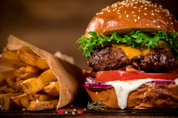 Tasty burger with french fries on wooden table.