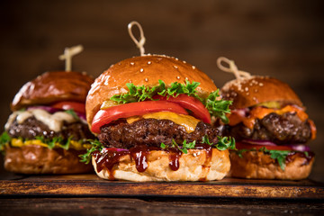 Tasty burgers on wooden table. - obrazy, fototapety, plakaty