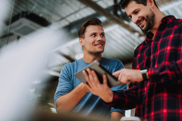 Low angle of joyful smart male colleagues using gadget while having a business talk