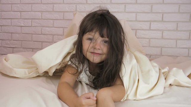 Cheerful child under the covers. The little girl is hiding under a blanket.