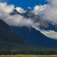 Clouds over the tops of the rocky mountains overgrown with trees. Photographed in the Caucasus, Russia.