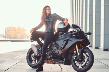 Plakat A beautiful biker girl leaning on her superbike outside a building.