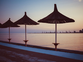Side view to beach straw umbrellas and sandy beach line. Albania. Sunset sky