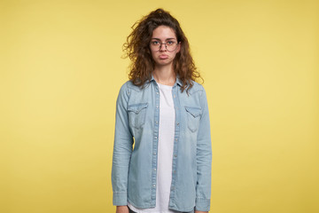 Displeased pretty brunette woman makes a funny disappointing face , isolated over yellow background