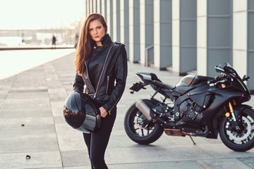 Obraz na płótnie Canvas A beautiful biker girl holding helmet next superbike outside a building.