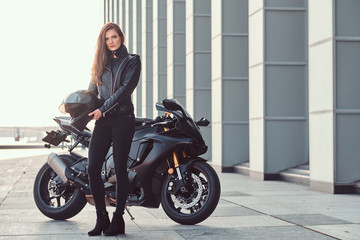 Fototapeta na wymiar A beautiful biker girl holding helmet next superbike outside a building.