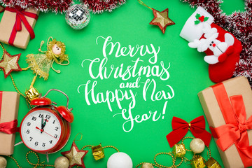 Fototapeta na wymiar Red alarm clock, Christmas decorations, Christmas toys and gift boxes on a green background. Added text Merry Christmas and Happy New Year. Flat lay, top view