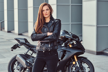 A confident biker girl with her arms crossed next to her superbike outside a building.