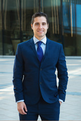 Portrait of happy confident businessman in blue suit in front of skyscrapper