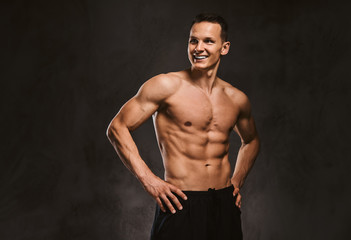Fototapeta na wymiar A handsome young fitness model with muscular body posing in studio on dark background.