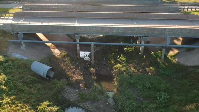 Aerial dolly shot of light traffic driving over a man made drainage canal or ravine crossover bridge on a bright sunny day.