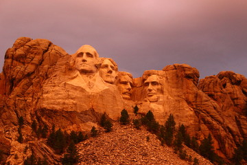 Mount Rushmore in the South Dakota Black Hills National Forest.  Summertime with the warm glow of an early evening sun shining on the president's faces - obrazy, fototapety, plakaty