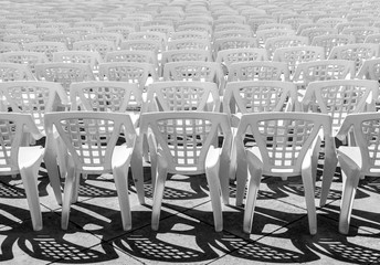 Vacant empty plastic white chairs pattern. White plastic chairs texture. Isolated View White Plastic Event Chairs Seating in Rows, Copy Space Use Overlay for Text. Black and white contrast made by sun