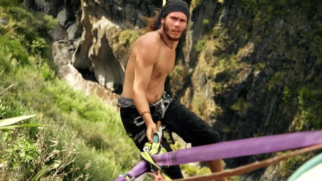 athletic male sitting on slackline or tightrope over green forest