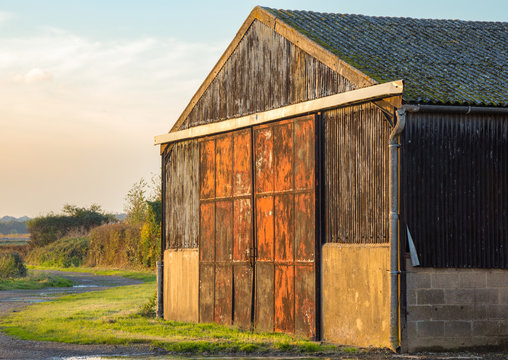 Barn on farmland with metal red and rusty doors.
