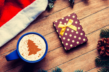 Cup of coffee and gift box with pine and hat on wooden table.