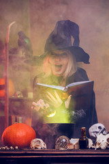 Photo of witch with pumpkin and book of spells at table with pot of steam