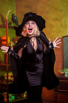Picture of screaming witch in black hat, dress on background of rack with pumpkin and crow in dark room