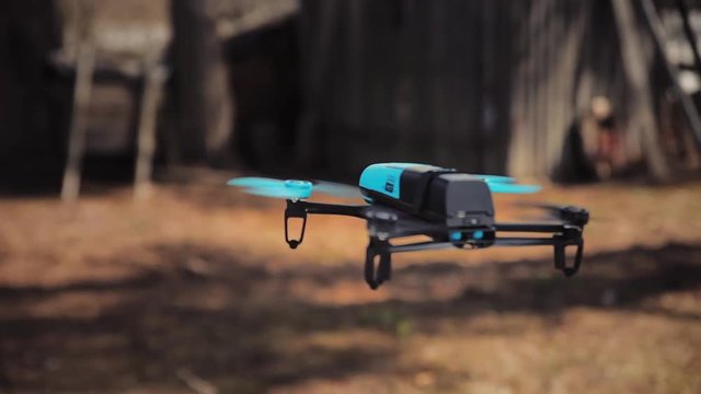 blue drone hovered in the air against the outbuildings