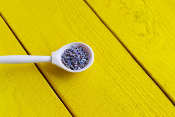 wooden spoon with dried lavender flowers on a yellow rustic wooden table