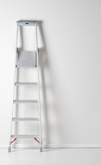 Single aluminum folding metal step ladder leaning against white plaster wall © Shawn Hempel