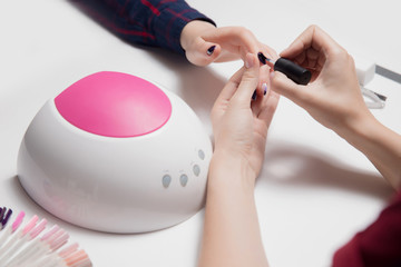 Pink led manicure lamp in foreground. Beautiful female hands apply gel Polish