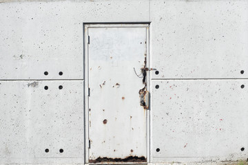A textured white metal door on a concrete wall. Outside at a train station.