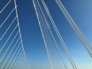 detail close up o fwhite steel bridge suspension wires against blue sky