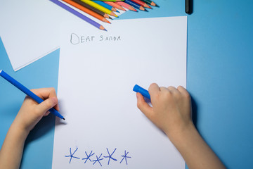 Little girl with pencils and felt-tip pens is writing a letter to Santa